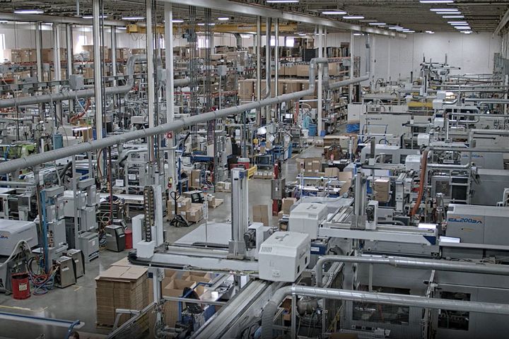 Fabrikhalle: Weitwinkelansicht einer modernen Fabrikhalle mit Reihen von automatisierten Spritzgussmaschinen, Rohrleitungen und gestapelten Materialien.