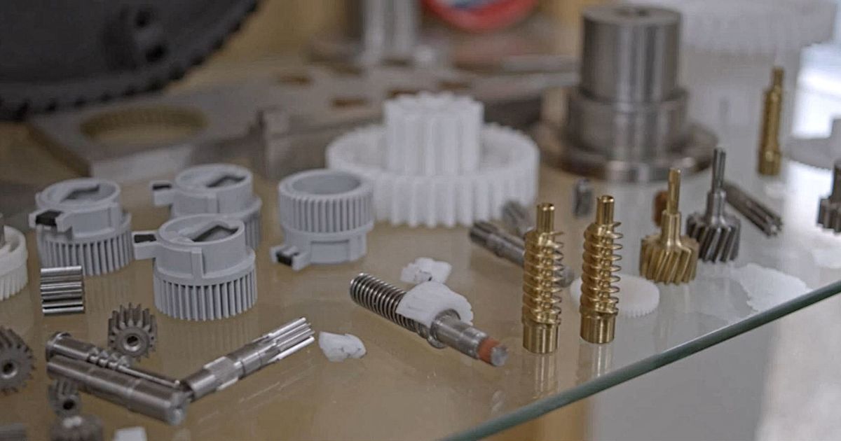 Close-up of a display of precision-machined components and plastic gears arranged on a glass surface.