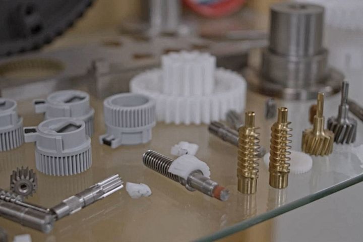 Präzisionsteile: Nahaufnahme einer Ausstellung von präzisionsgefertigten Bauteilen und Kunststoffzahnrädern, die auf einer Glasfläche angeordnet sind.