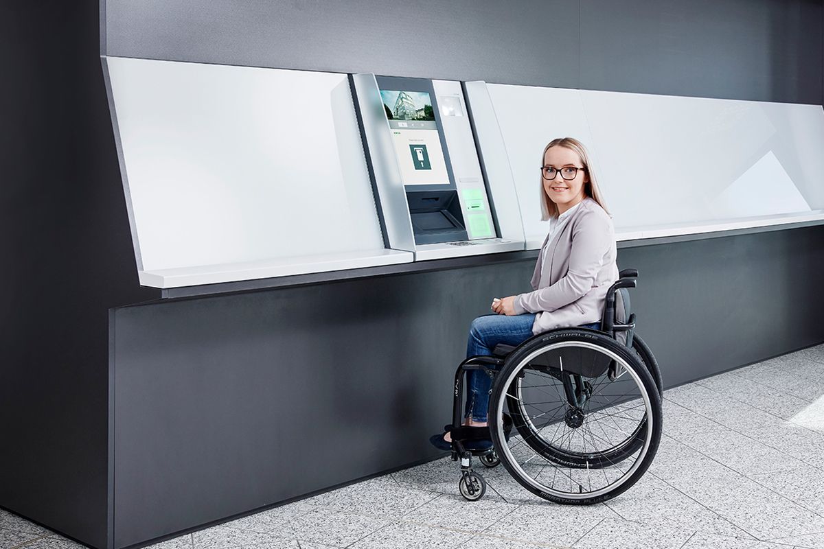 Junge Frau im Rollstuhl vor einem unterfahrbaren KEBA Cash Recycler