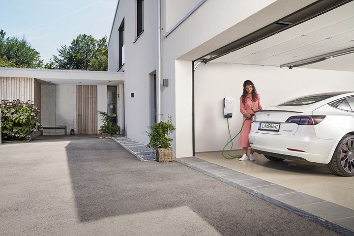 Voiture électrique en cours de recharge sur une borne murale dans le garage d’une maison individuelle.