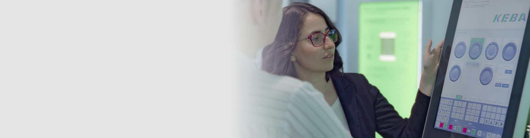 A female employee explains an industrial control system to a colleague using a modern touch panel with KEBA’s user interface.