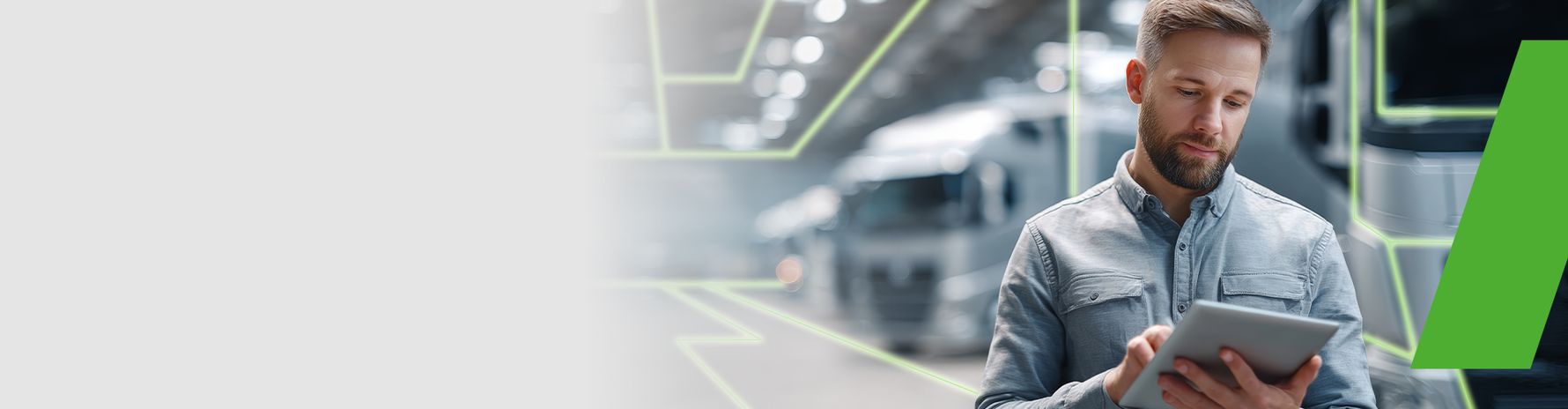 Man working with a tablet in a modern industrial setting; trucks and digital lines visible in the background.