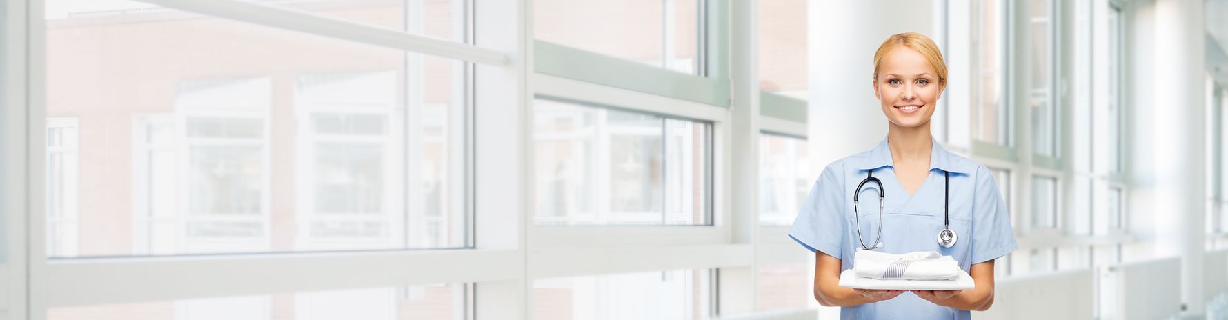 Smiling nurse with a stethoscope holding folded clothes.