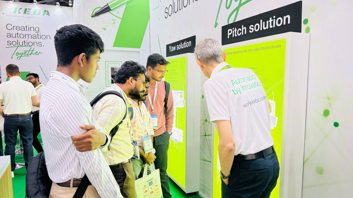Group photo of KEBA team members standing together at a trade fair booth. The background shows the KEBA exhibition stand with white and green branding.