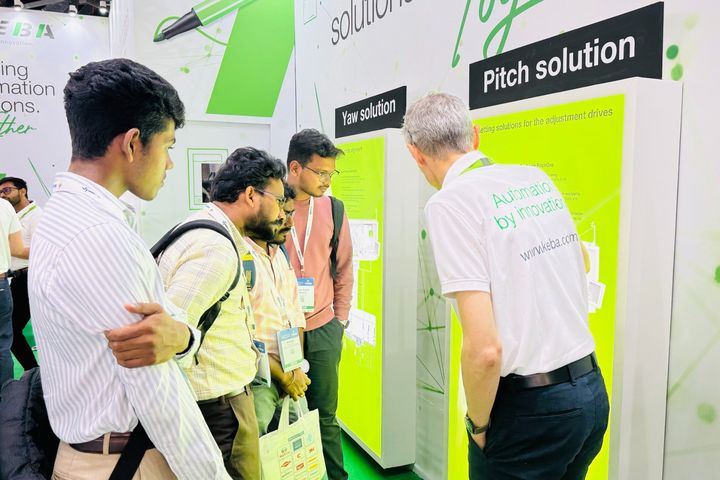Group photo of KEBA team members standing together at a trade fair booth. The background shows the KEBA exhibition stand with white and green branding.