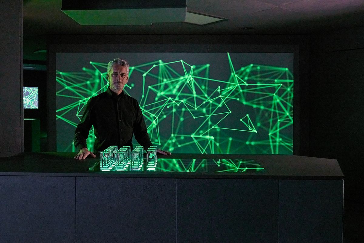 Thomas Linde stands in the KEBA InnoSpace in front of an impressive digital projection of glowing network structures – a symbol of future vision, technological expertise, and interactive experiences.