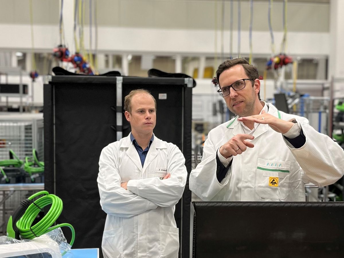 Two men in white lab coats discussing in a production setting with KEBA components.