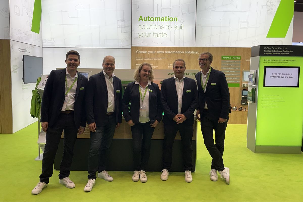 KEBA team group photo in front of the company’s exhibition booth. The background highlights KEBA’s automation solutions and displays with interactive screens and green-themed elements. The team is smiling and dressed in coordinated business attire with KEBA name tags.