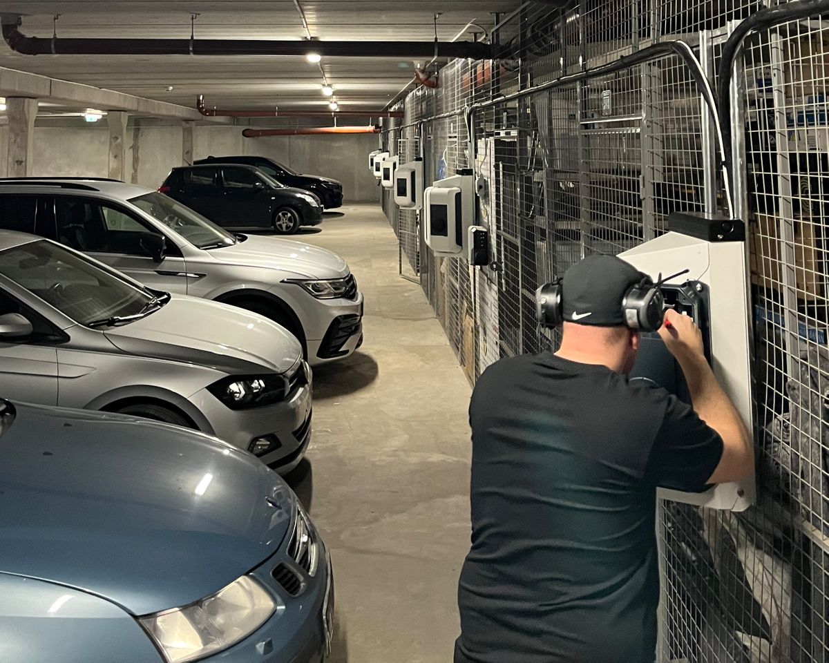 A technician installs a KEBA wallbox in an underground garage between parked vehicles.