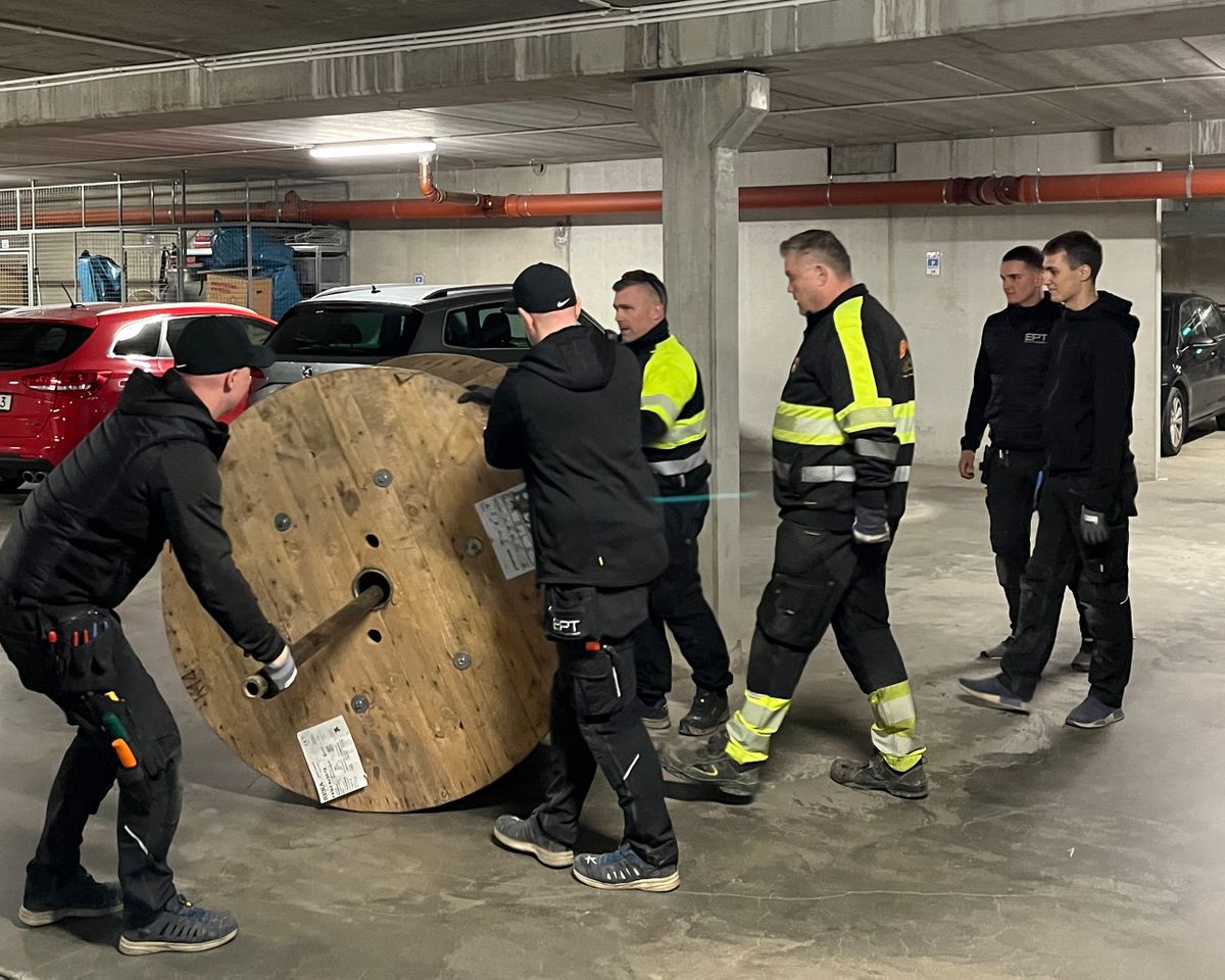 Six workers move a large cable drum in an underground garage.