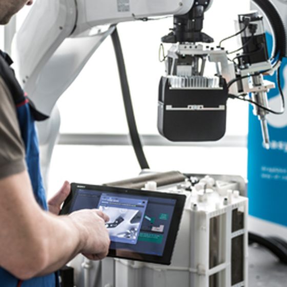 A person controls an industrial robot using a tablet.