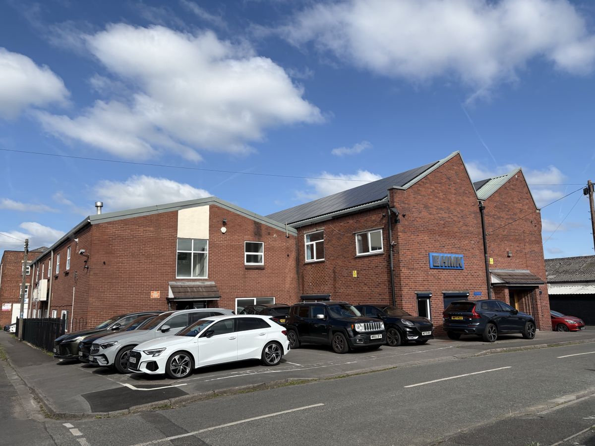 HMK Headquaters in Cheshire, UK - a brick industrial building with parked cars in front of it, under a blue sky with clouds.