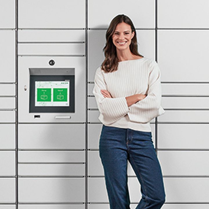 Frau steht lächelnd, mit verschränkten Armen vor einer KEBA-Paketstation