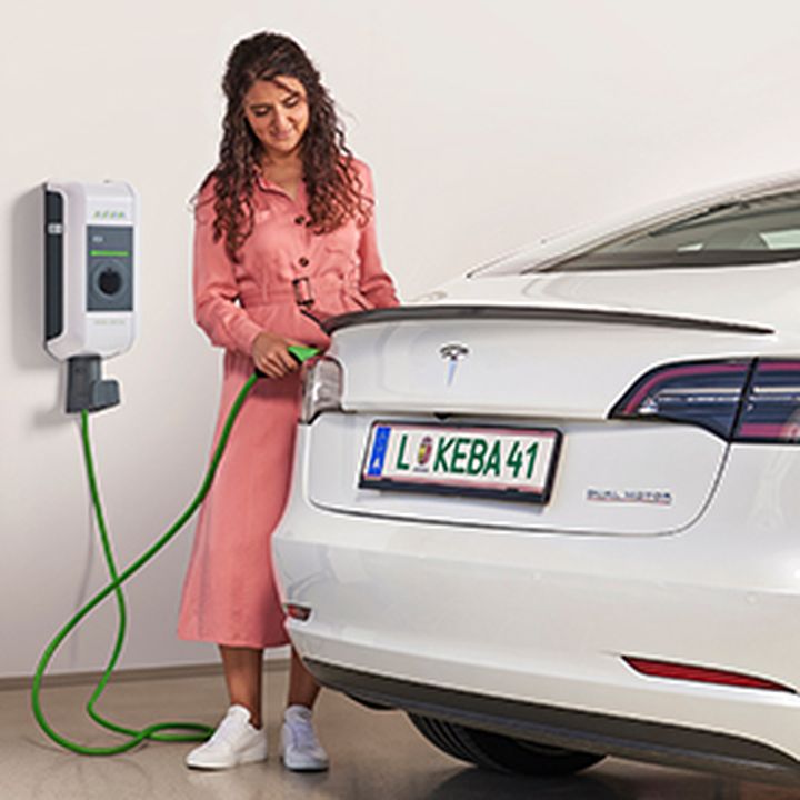 Frau steckt das grüne Kabel ihrer KEBA-Wallbox in ihr Auto um es zu laden.