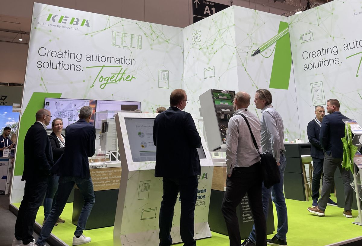 Two men are standing at the KEBA booth, reviewing documents together in front of the drag&bot display.