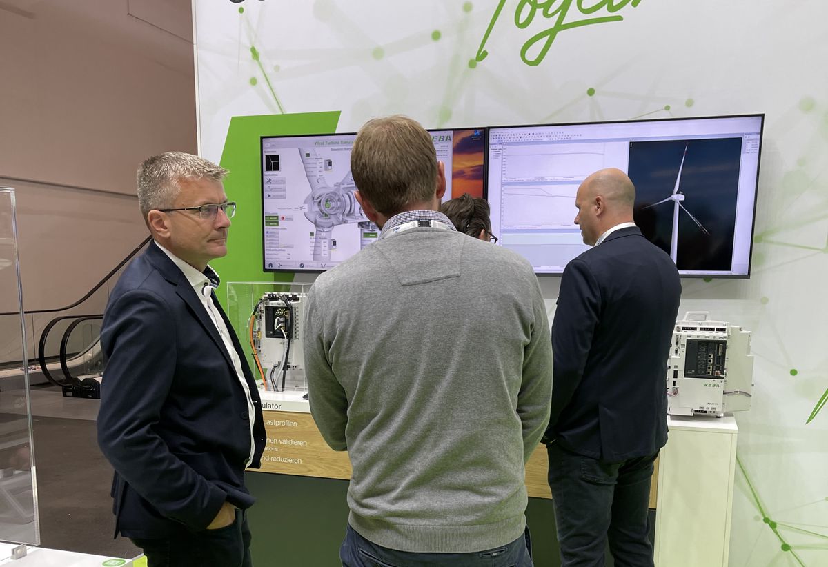 A man demonstrates KEBA’s industrial automation equipment to a visitor in front of a screen at a trade fair.