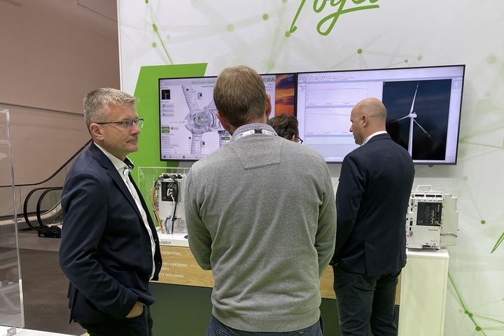 A man demonstrates KEBA’s industrial automation equipment to a visitor in front of a screen at a trade fair.