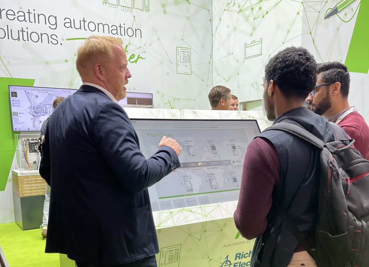 Several people observing a demonstration of a pick-and-place application with Kemro X at a KEBA trade fair booth.