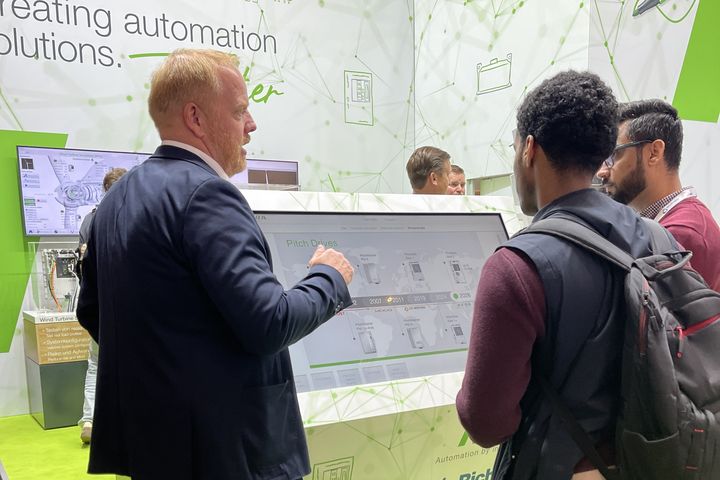 Several people observing a demonstration of a pick-and-place application with Kemro X at a KEBA trade fair booth.