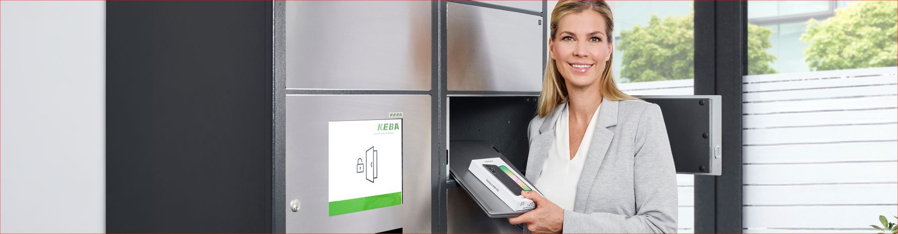 Eine blonde Frau entnimmt einen Laptop und ein verpacktes Handy aus einer Übergabestation.