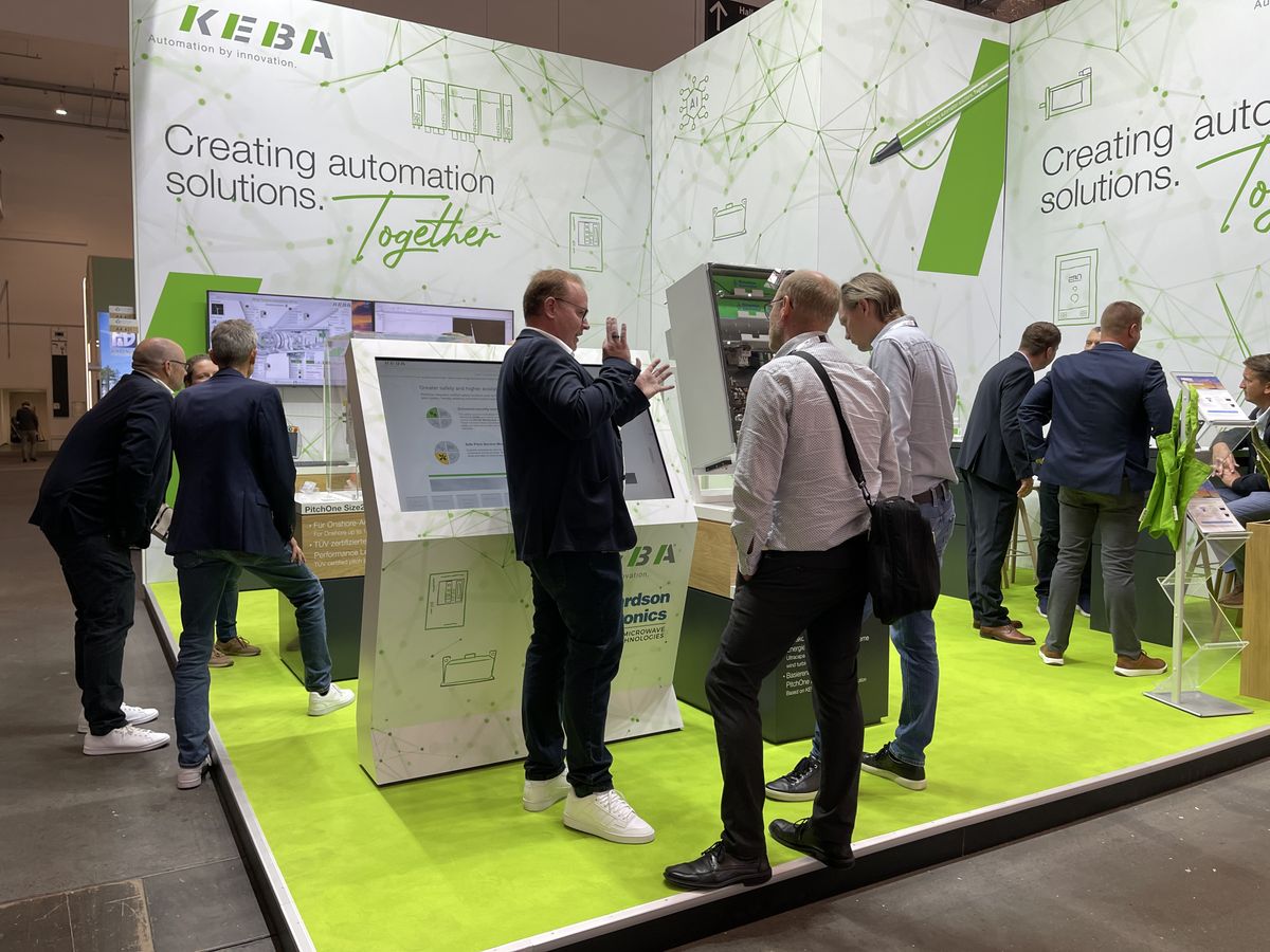 Three people stand at the KEBA booth in front of the drag&bot display, discussing a robotics solution.