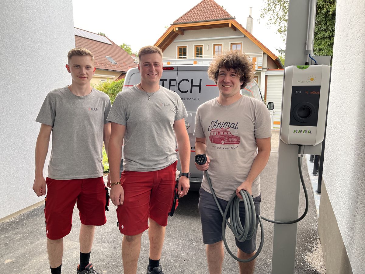 Drei junge Männer stehen neben einer KEBA-Wallbox – die Installation ist abgeschlossen.