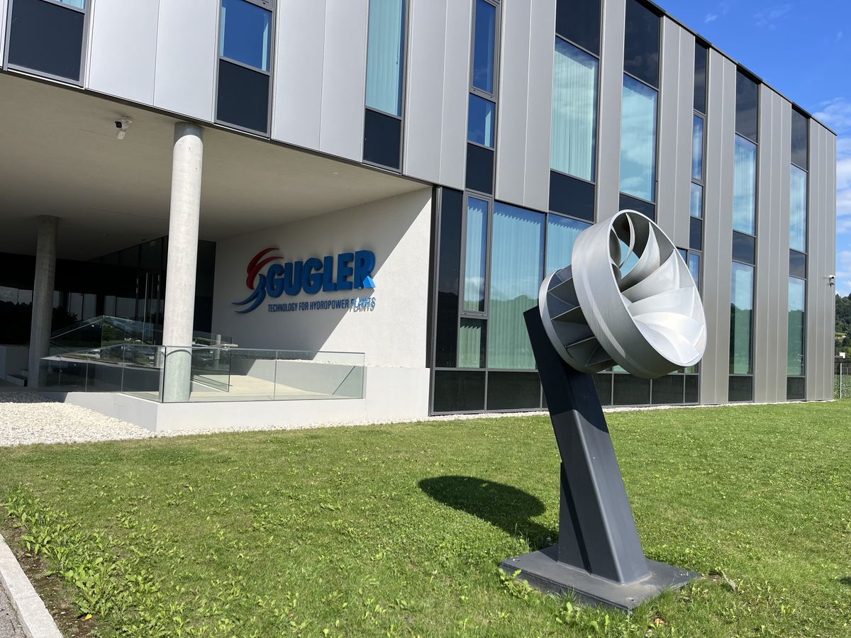 Unternehmensgebäude von GUGLER mit moderner Wasser­turbine auf dem Rasen davor.