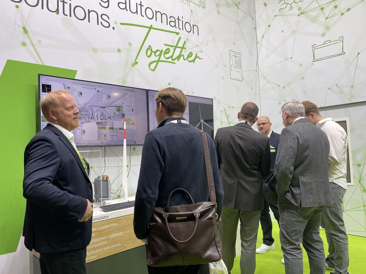 Three men are having a conversation at the KEBA booth in front of a screen displaying information about the Kemro X platform.