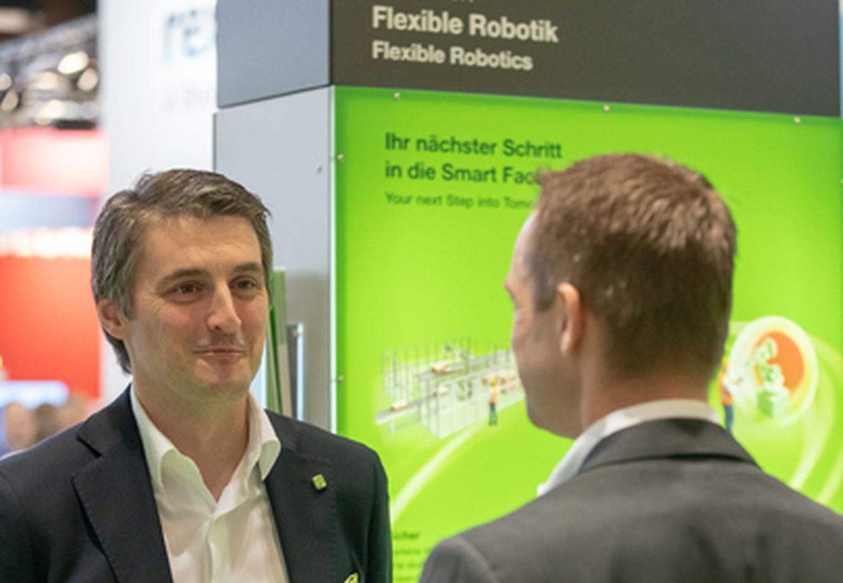 Two people engaged in a professional discussion at a trade fair booth about flexible robotics and smart factory solutions.