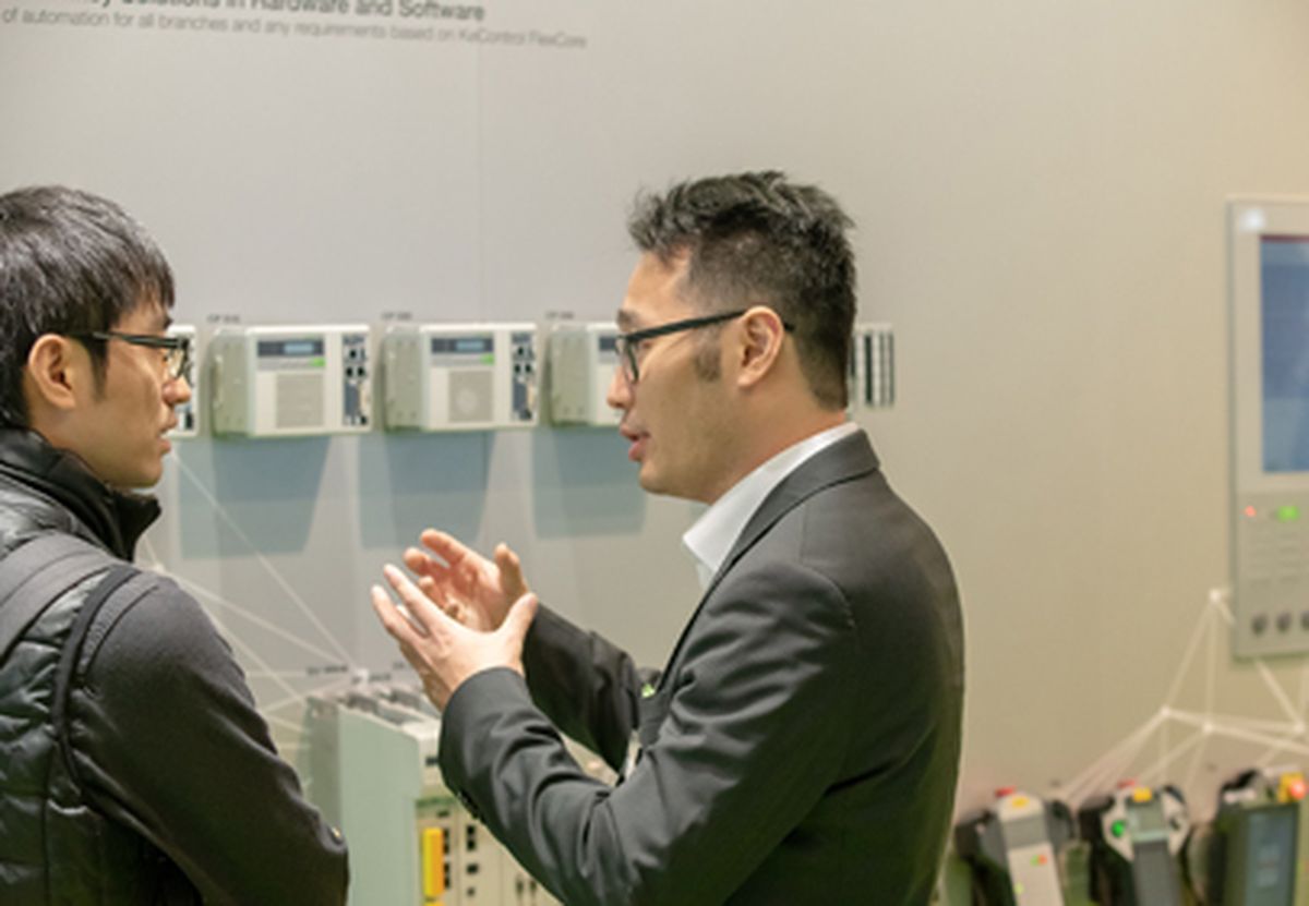 Two people having a technical consultation in front of displayed automation and control systems at a trade fair booth.
