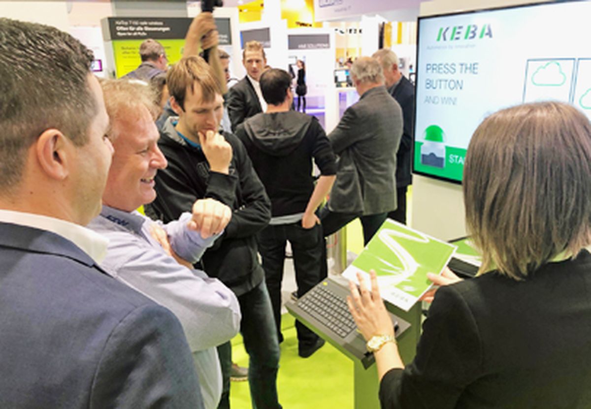 Visitors watching an interactive demonstration of an automation solution at a trade fair booth, where functions are explained and tested using an operator device.