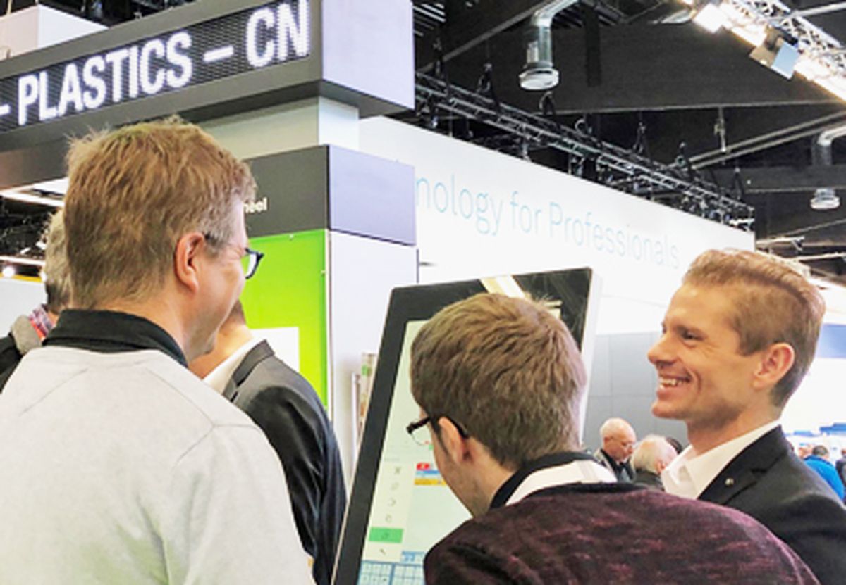 Several people at a trade fair booth discussing automation solutions using an interactive visualization or display.