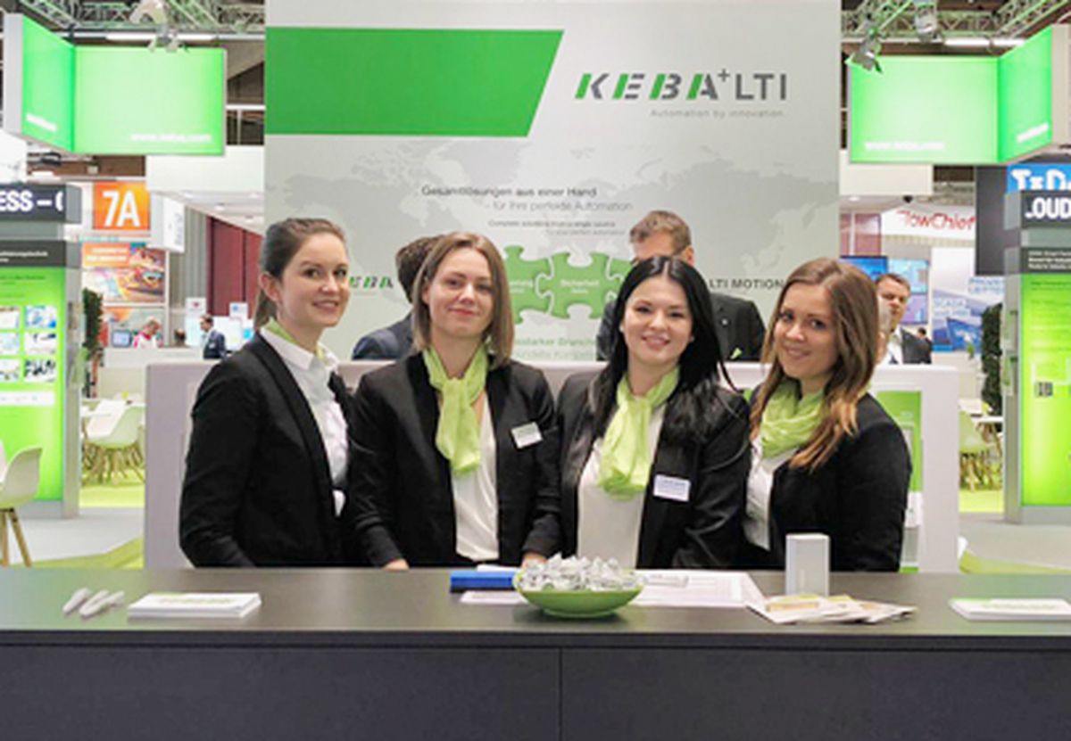 Several employees standing behind the counter of a KEBA trade fair booth, welcoming visitors and serving as a point of contact for information and consultation on automation solutions.
