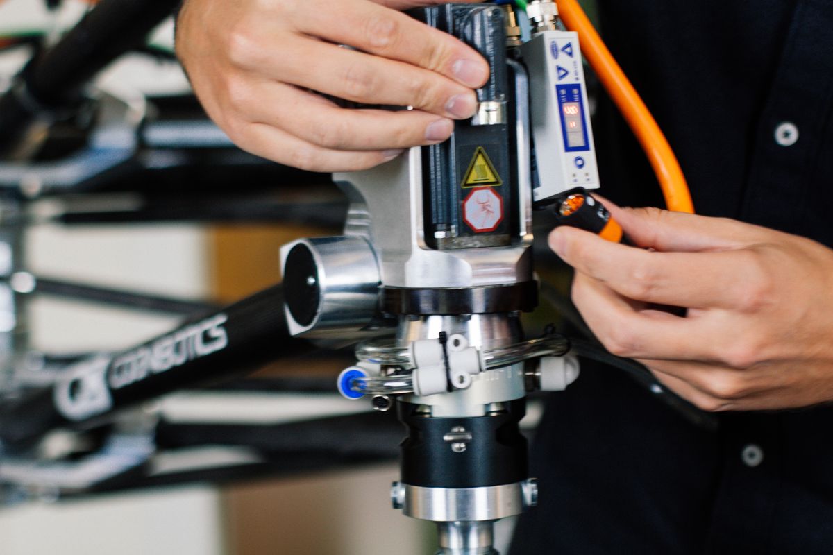 Detailaufnahme eines Industrieroboters mit Präzisionsgreifer, der über eine Steuerkonsole bedient wird, während Kunststoffboxen für automatisierte Sortierprozesse bereitstehen.