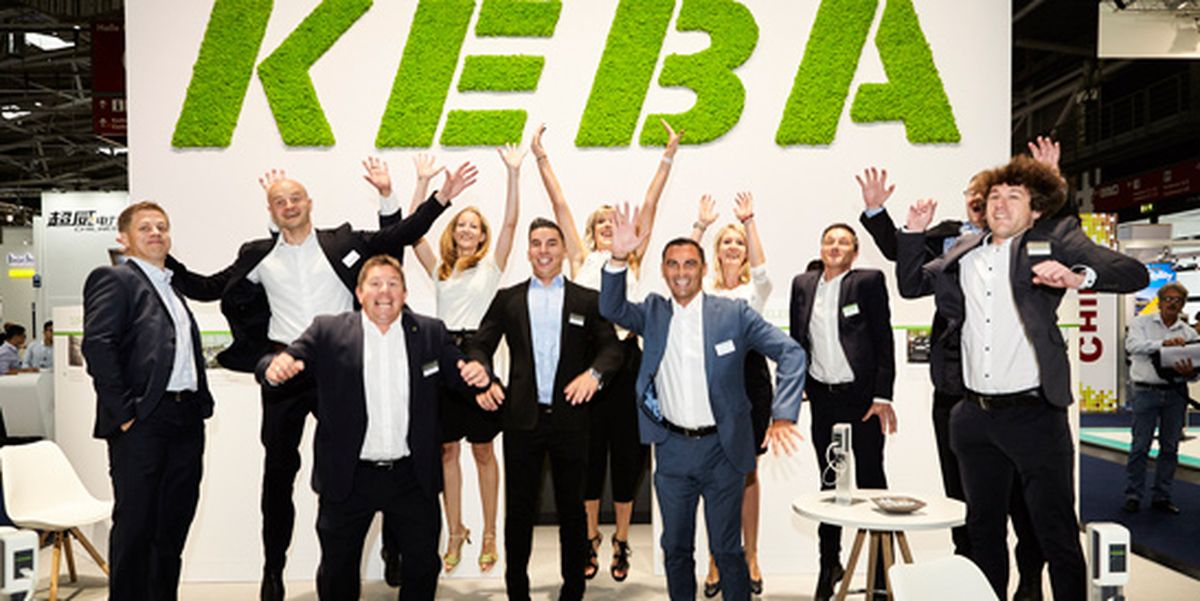 The KEBA trade fair team celebrates together in front of a large company logo made of green moss – full of energy and team spirit at the exhibition.