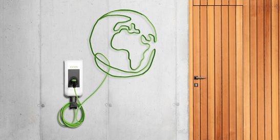 KEBA wallbox mounted on a concrete wall, with the green charging cable forming a globe – symbolizing global sustainability and e-mobility.