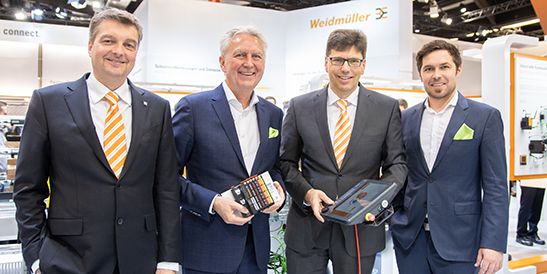 Several people standing together at a trade fair booth presenting industrial automation components and operator devices as part of a partner or customer showcase.