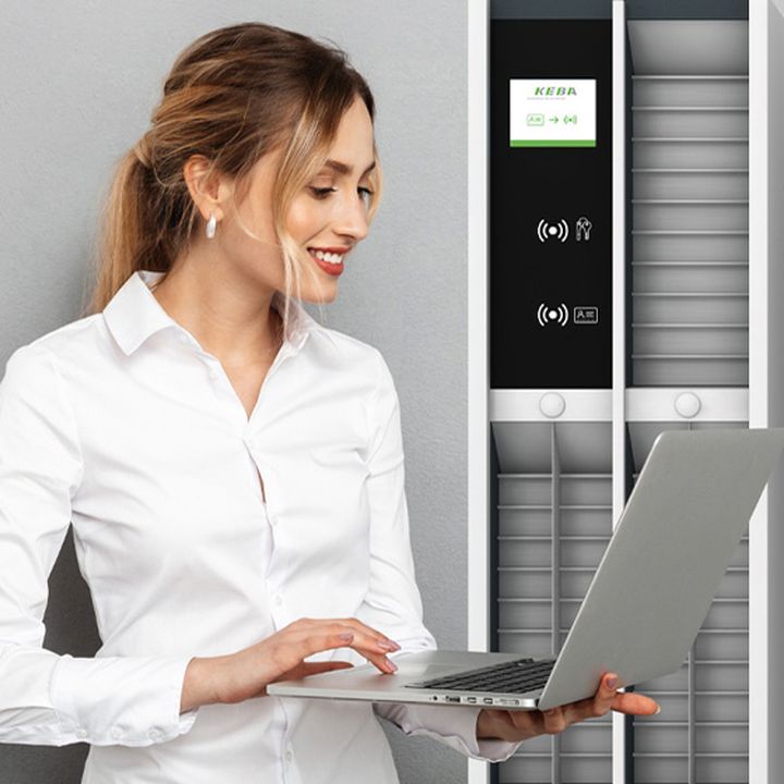 A woman in a white shirt smiles while using a laptop, standing next to a modern black and white locker system.