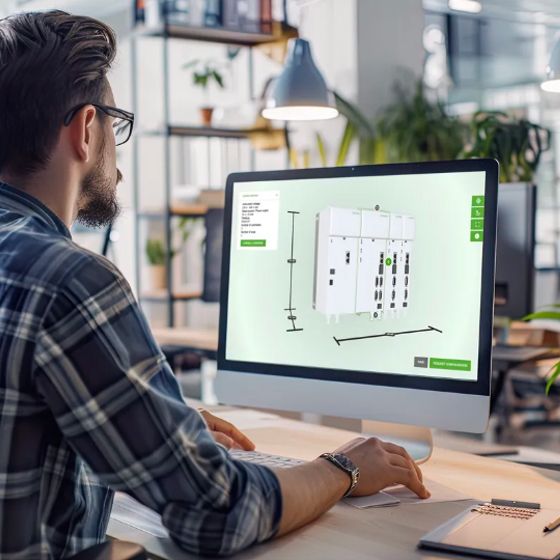 A man in a plaid shirt works on a computer displaying a 3D model of drives in a modern office setting.