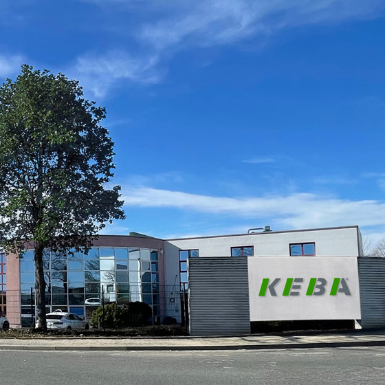 Company building with glass windows, a tree nearby, and "KEBA" sign on a large wall. The sky is clear and blue.
