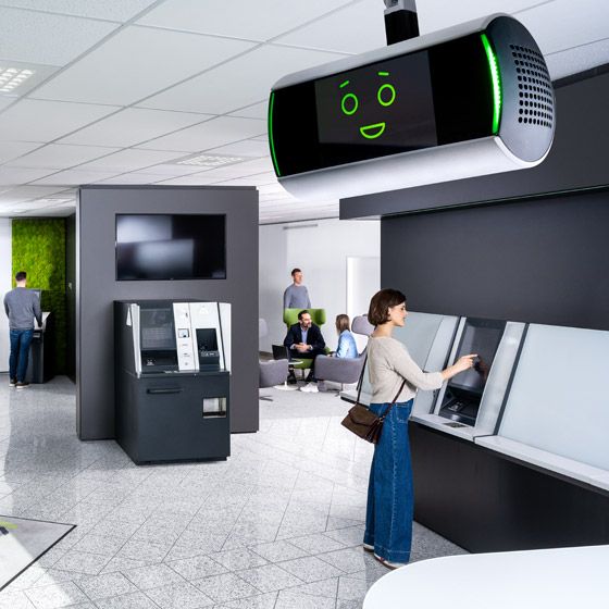 A modern bank interior with people using ATMs and our AI assistant KeBob on the ceiling.