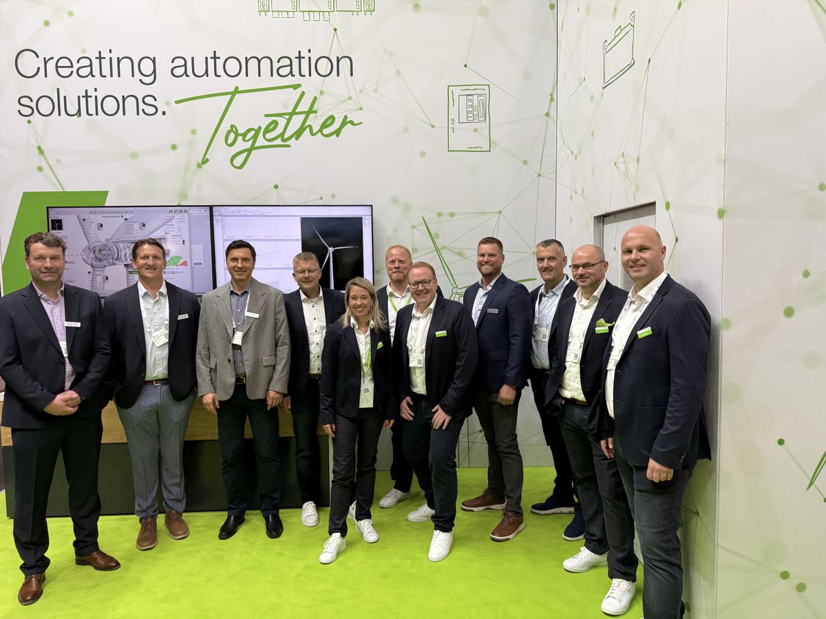 Drei Männer begutachten eine Roboterzelle am KEBA-Messestand. Einer erklärt technische Details und zeigt durch die Scheibe auf den Roboterarm.