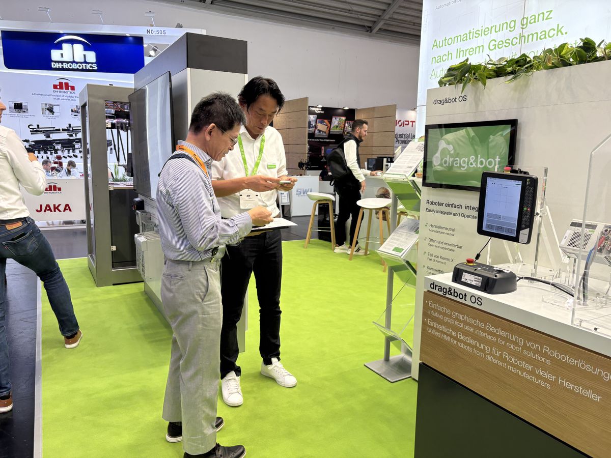 Zwei Männer stehen am KEBA-Messestand und betrachten gemeinsam Unterlagen vor dem drag&bot-Display.