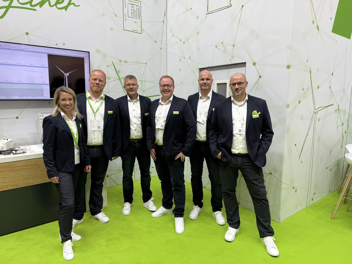 Group of KEBA employees standing together at a trade fair booth with presentation screen and automation solutions.