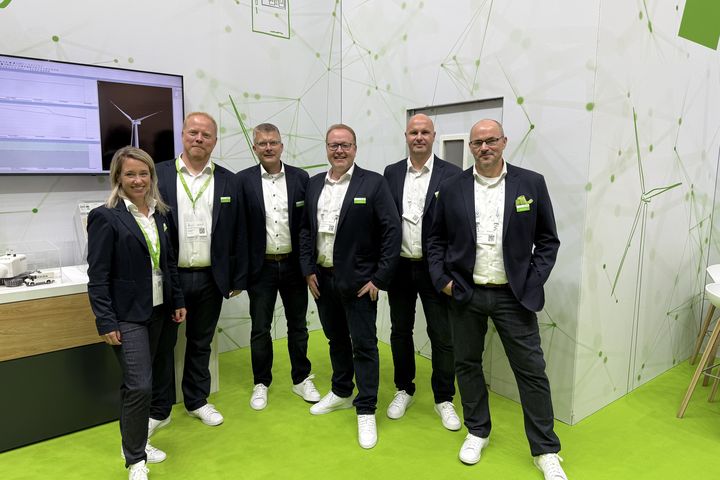 Group of KEBA employees standing together at a trade fair booth with presentation screen and automation solutions.