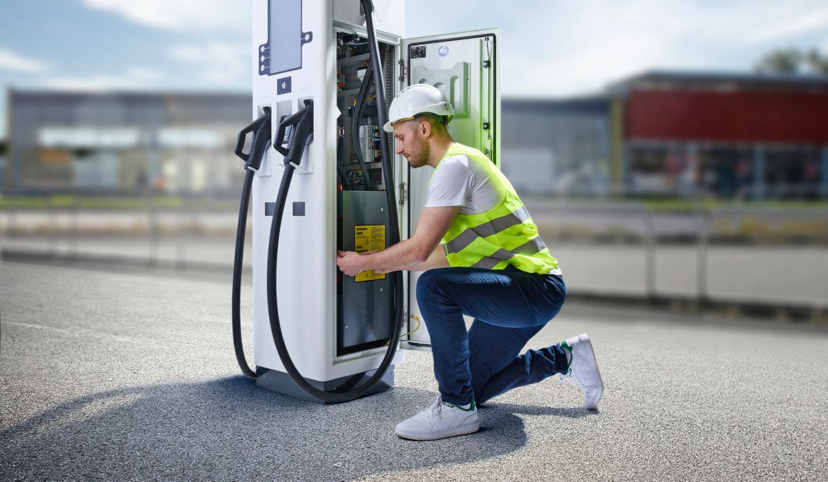 Service technician kneeling to repair a DC fast charging station