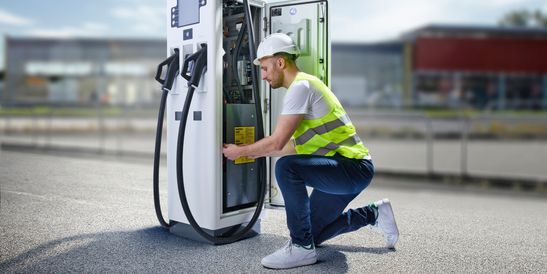Service technician kneeling to repair a DC fast charging station