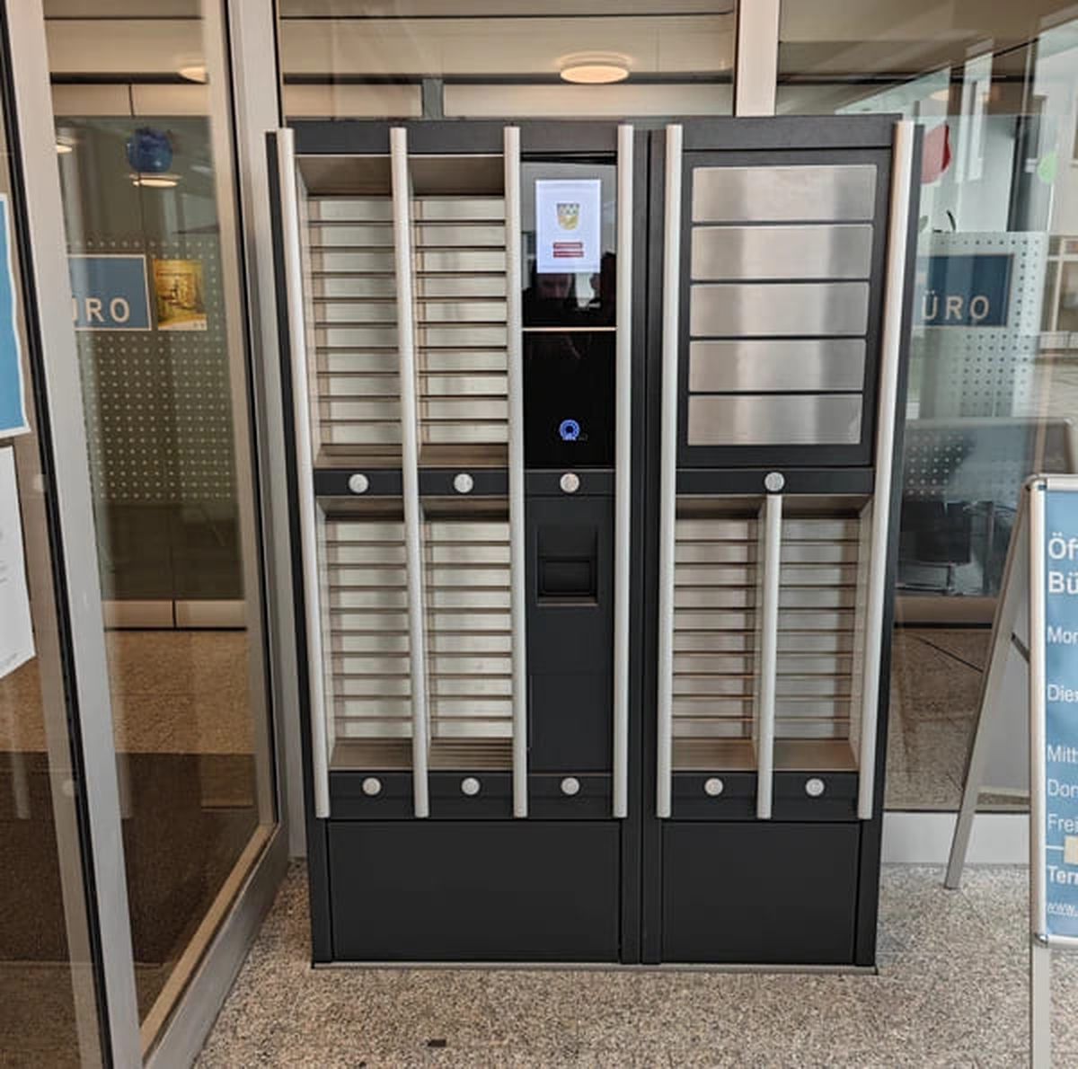 Self-service terminal with delivery compartments in front of a citizen office entrance.