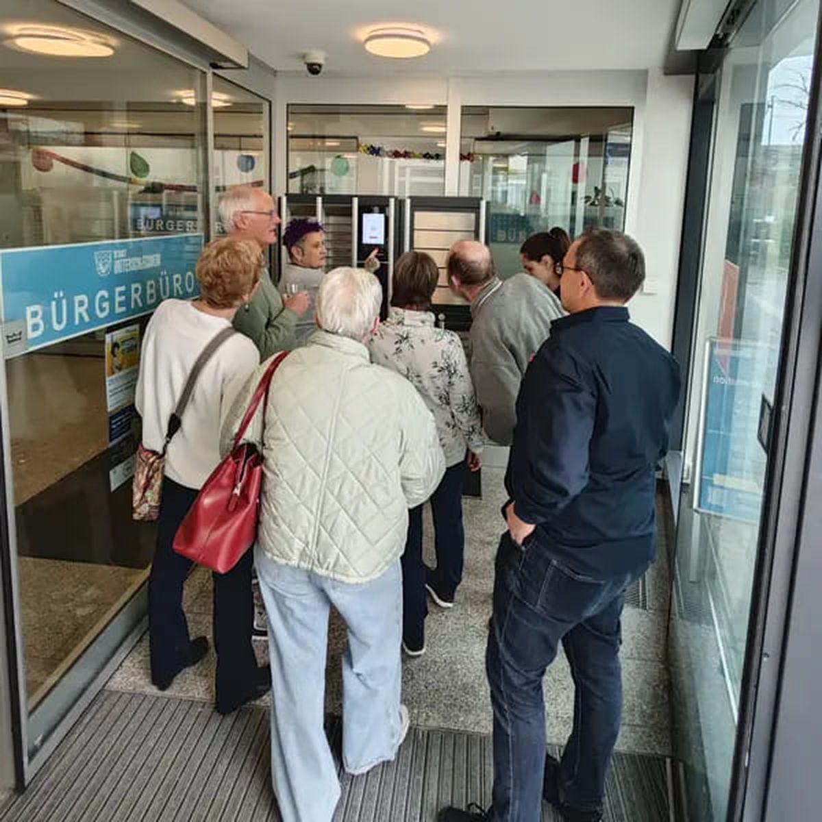 Several people stand at the entrance of a citizen office, looking at a screen.